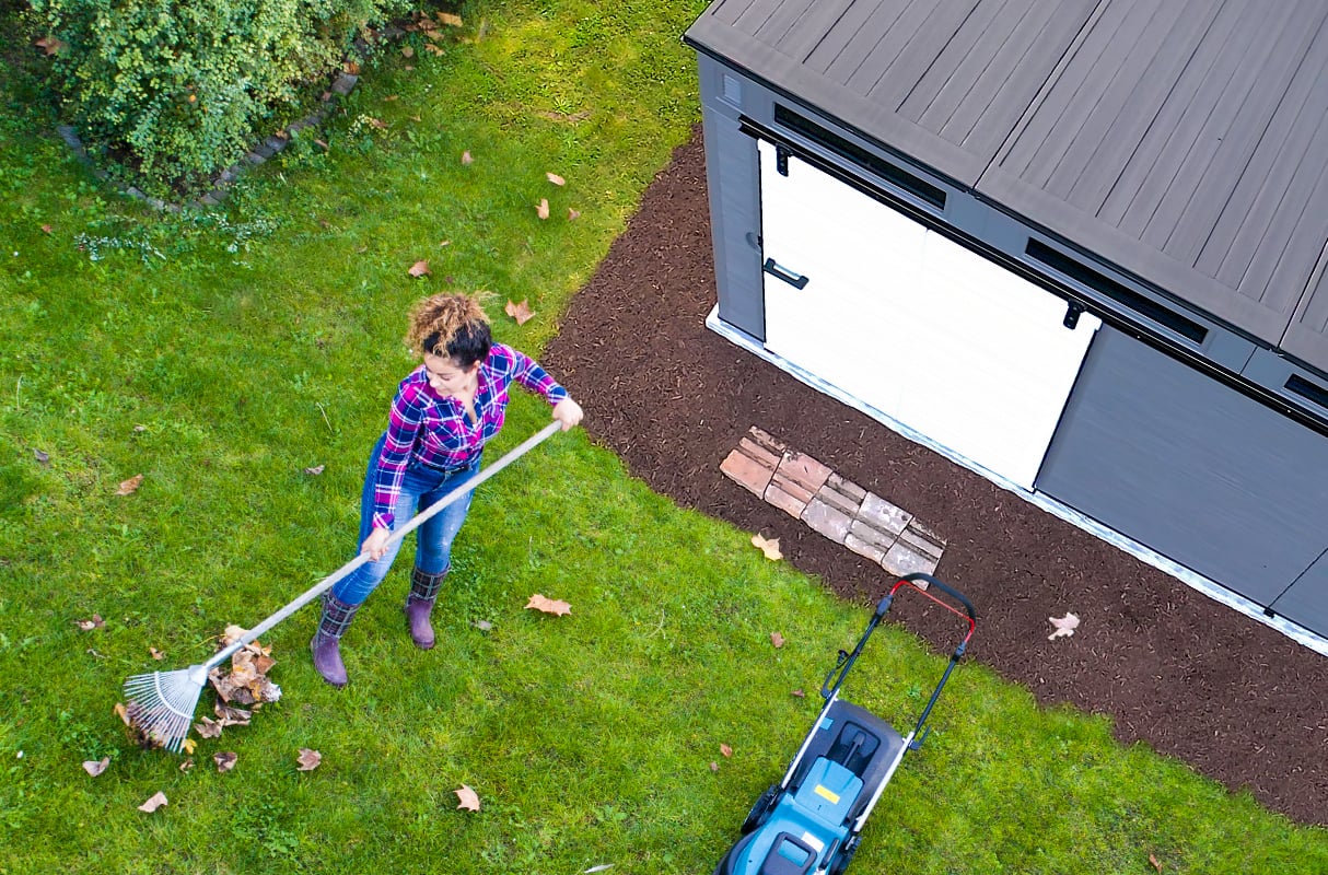Overhead shot of a woman raking leaves in front of a Suncast barn door shed