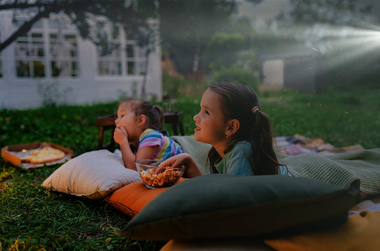 Two girls on pillows in their backyard watching a movie